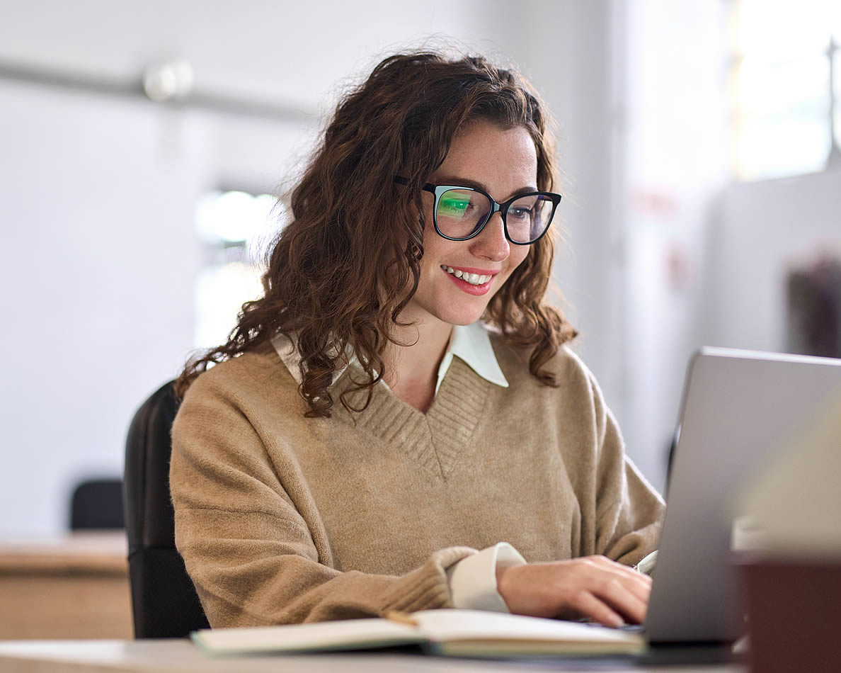 Frau sitzt an einem Bürotisch und tippt auf einem Laptop