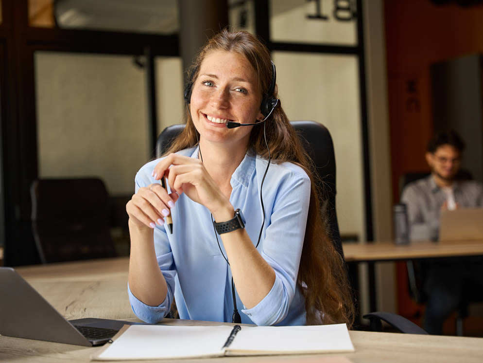 Junge Frau sitzt mit einem Headset an einem Bürotisch