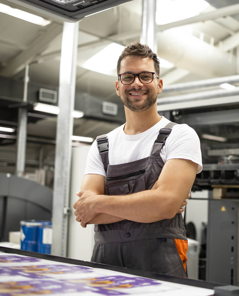 Lächelnder Mann steht vor einer Produktionsmaschine