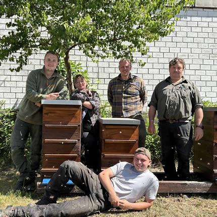 Fünf Personen posieren neben mehreren Bienenstöcken